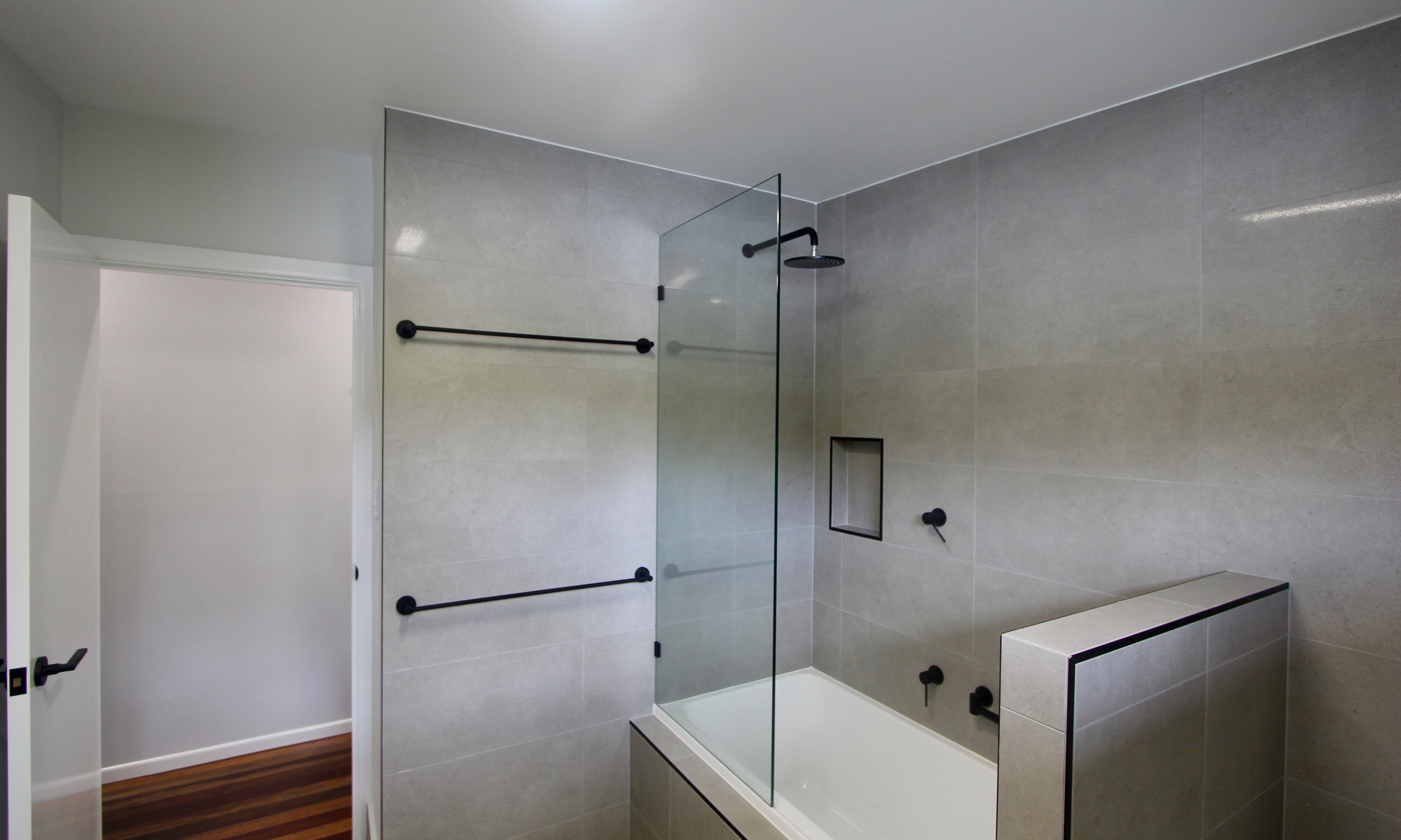 Frameless glass shower screen over bath with black accessories in Bathroom at The Gap 