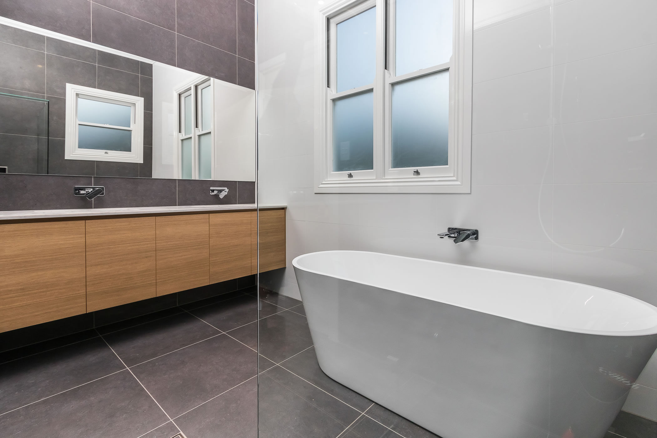 Bathroom with freestanding bath and large mirror above floating vanity