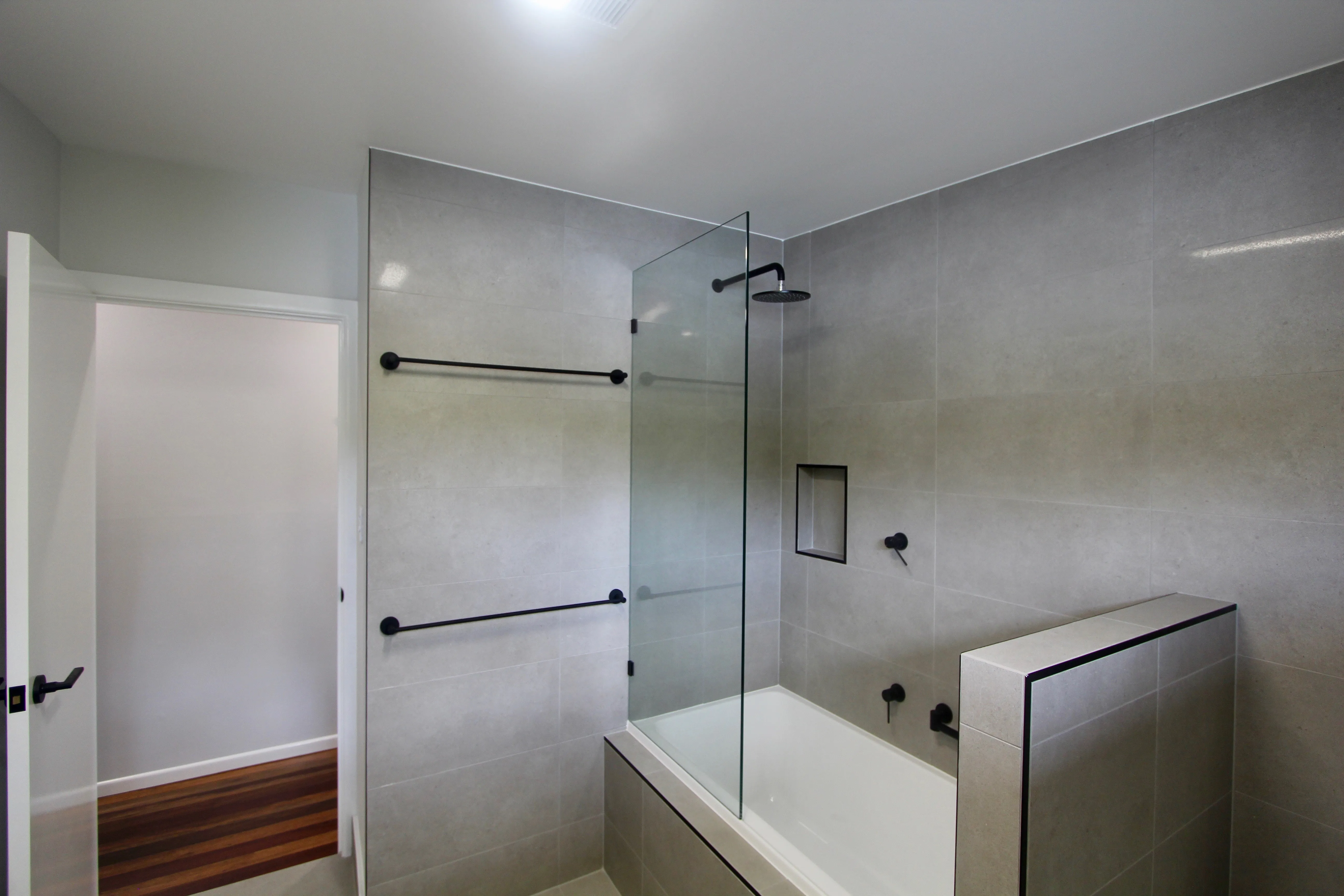 Frameless glass shower screen over bath with black accessories in Bathroom at The Gap 
