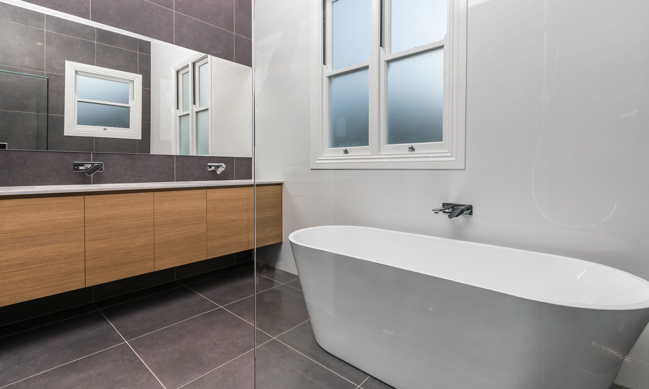 Bathroom with freestanding bath and large mirror above floating vanity